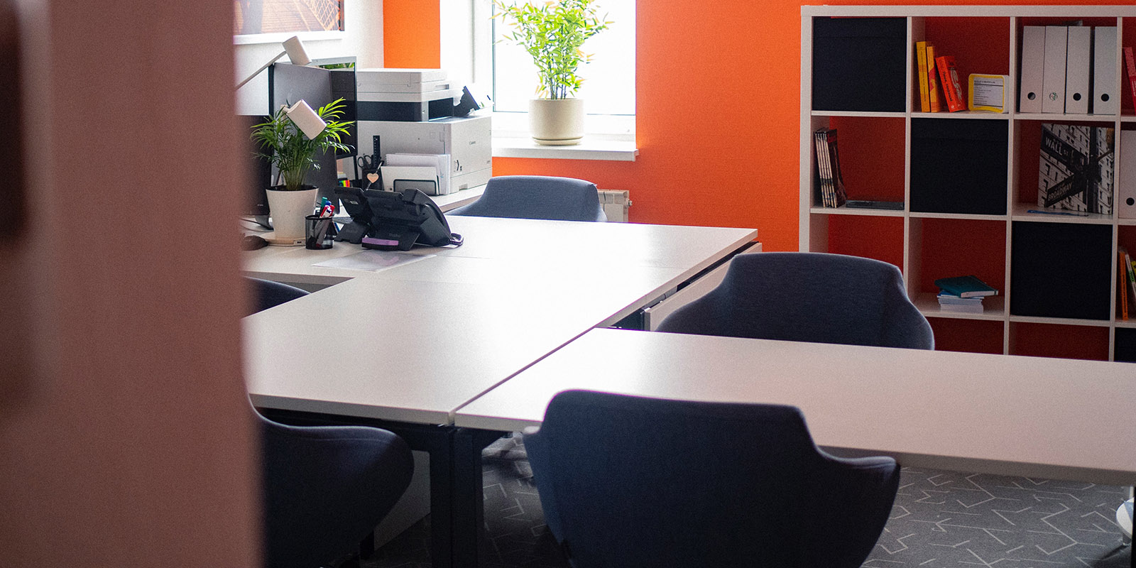 Office interior with large desk, shelving, orange walls and dark chairs